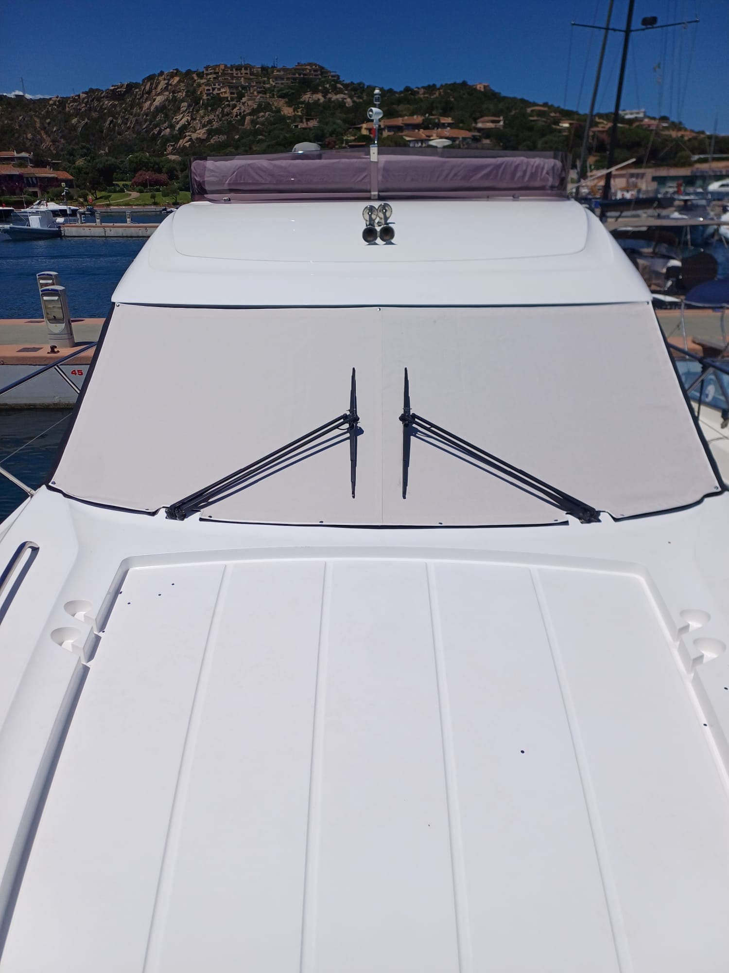 Copriparabrezza beige su motoscafo, vista da prua con porto sullo sfondo