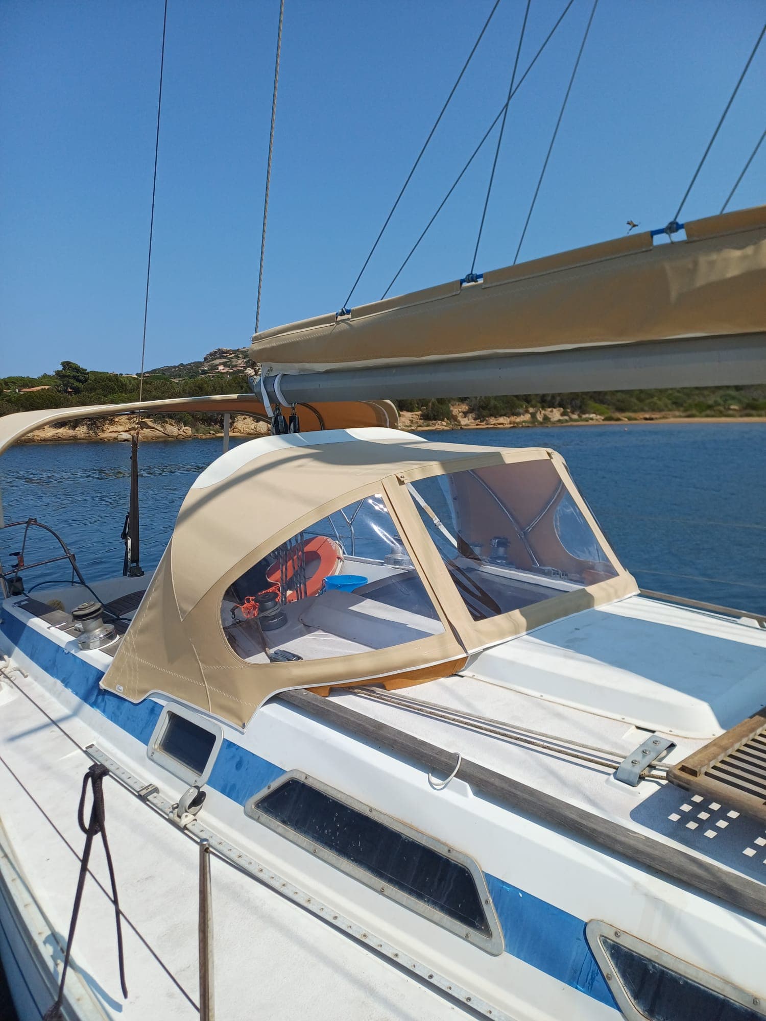 Sprayhood beige su barca blu, acque turchesi e macchia mediterranea