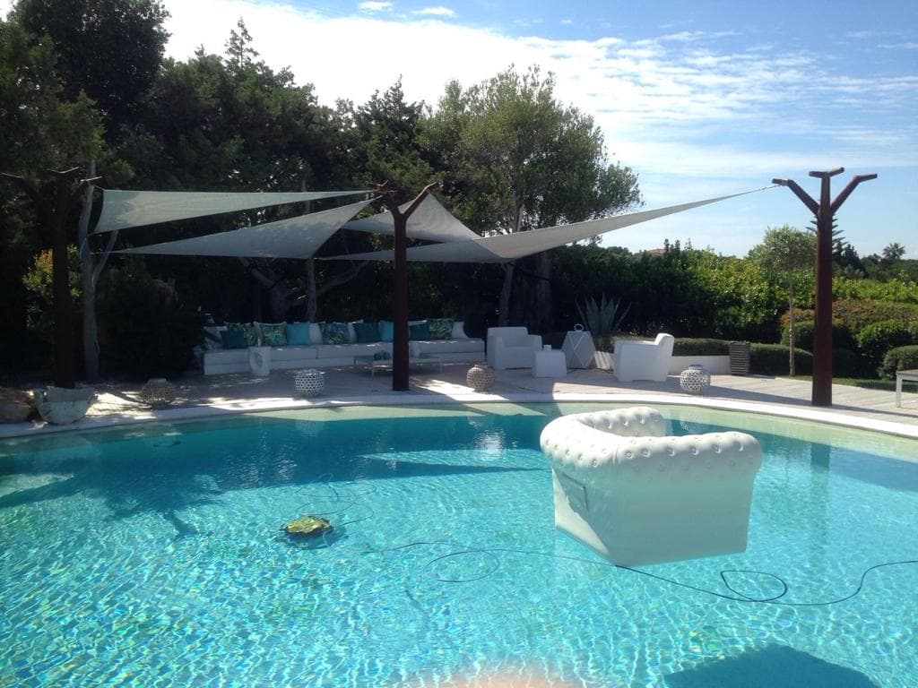 Vele triangolari su pali in legno naturale sopra piscina con divani bianchi